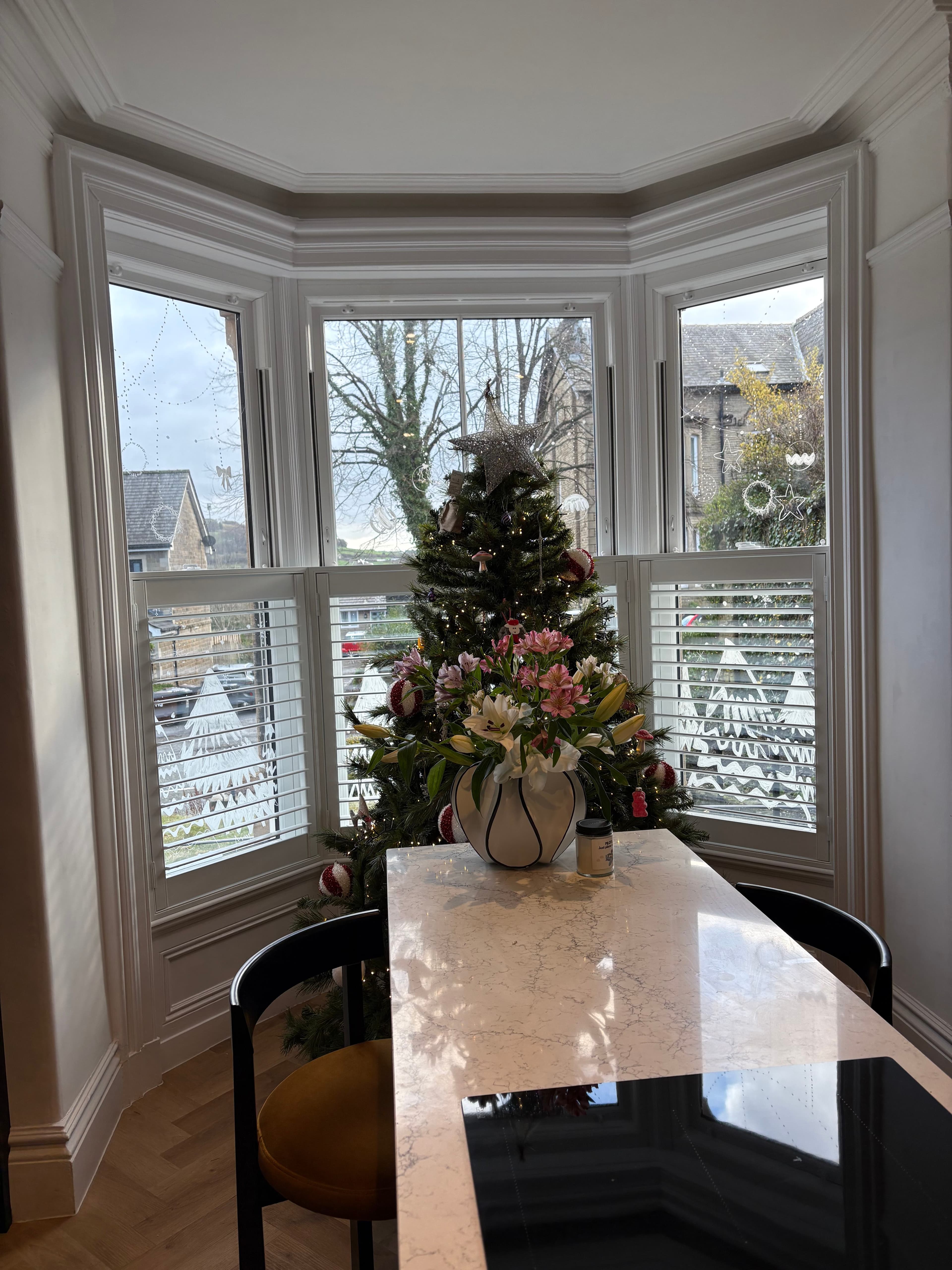 Half-height cafe-style white shutters in a bay window behind a dining table