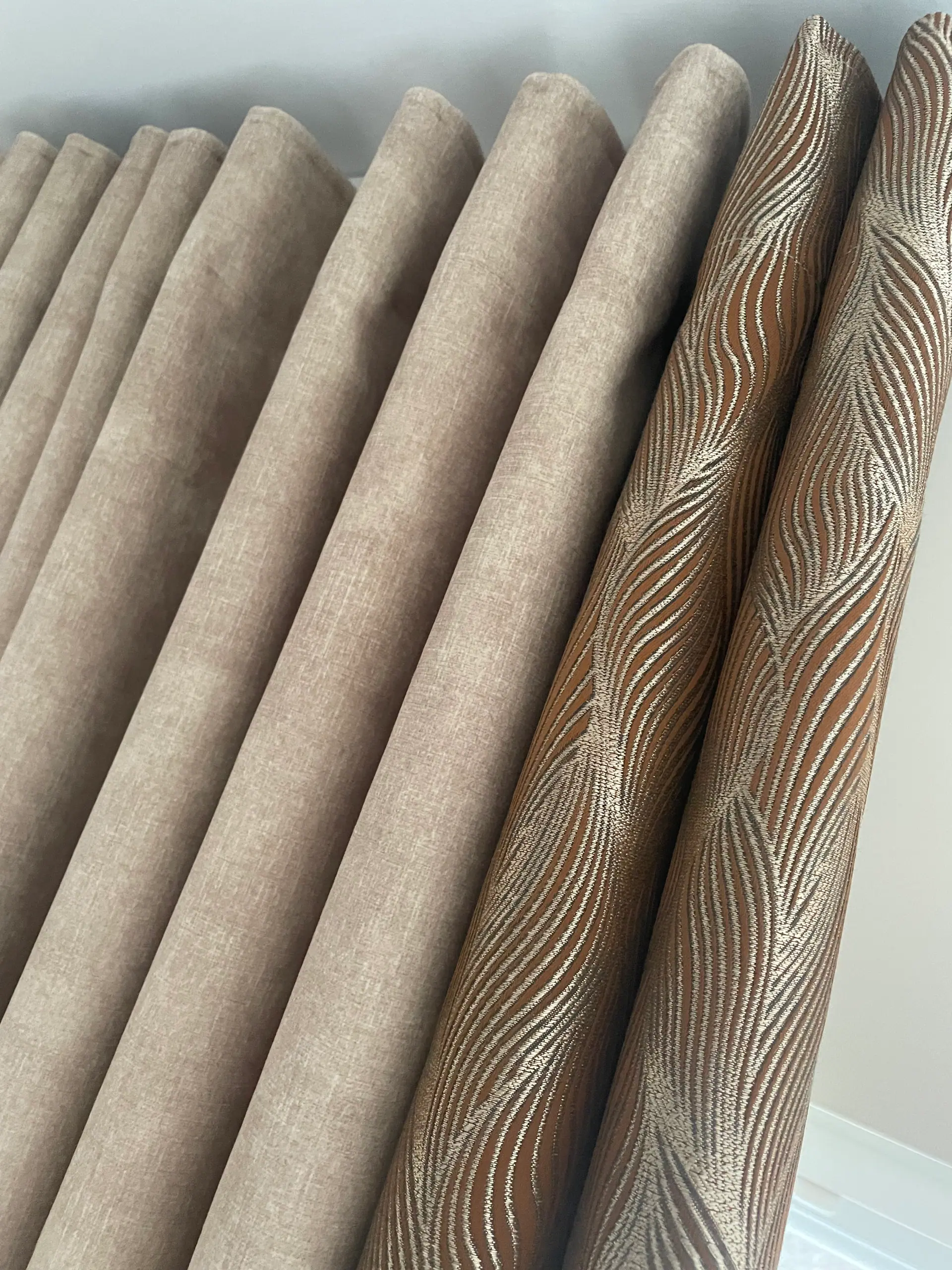 Close-up of beige wave-fold curtains beside a bronze patterned fabric